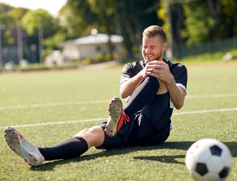 man on soccer field holding his knee in pain, seeking chronic pain management