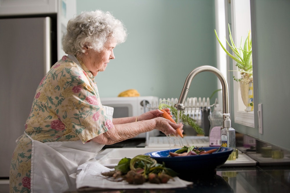 older woman washing vegetables at the sink benefiting from low-dose naltrexone